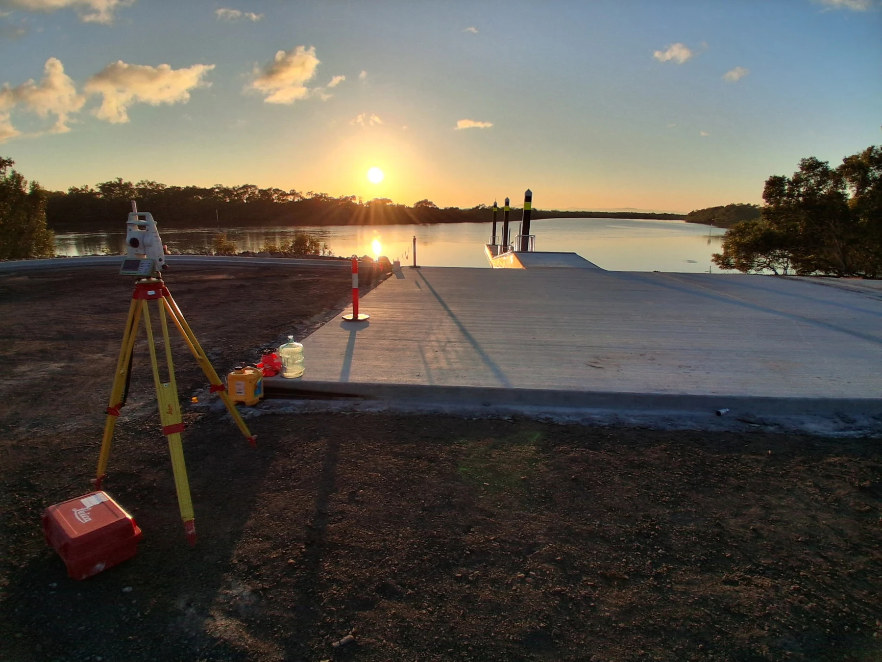 Survey equipment operating beside completed civil works at sunset